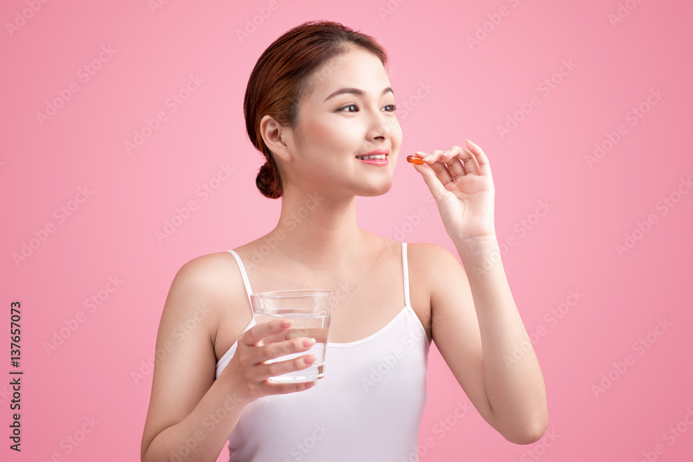 Young asian beauty young woman eating pills and drinking water on pink background. Young asian beauty young woman eating pills and drinking water on pink background.
