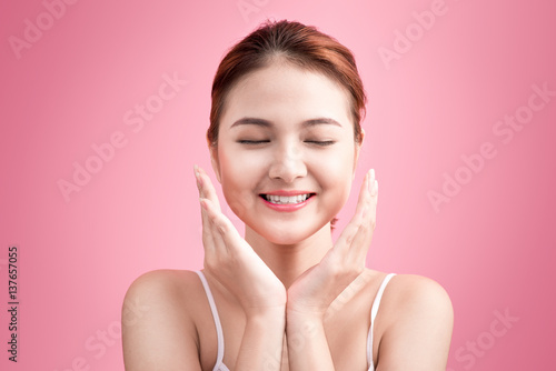 Smiling woman taking care of her face for fresh healthy skincare on pink background