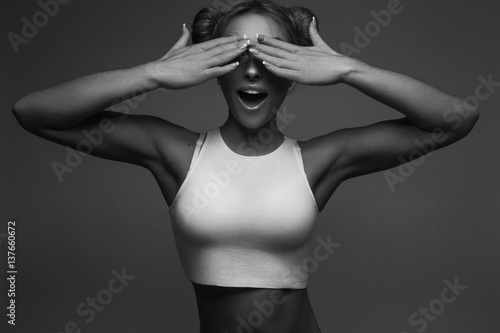 Спортивная девушка закрывает глаза руками и удивленно улыбается (черно-белая фотография)  photo