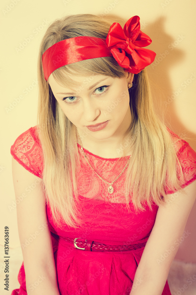 Naklejka premium Pretty blond woman in red outfit with ribbon in hair lying on fur