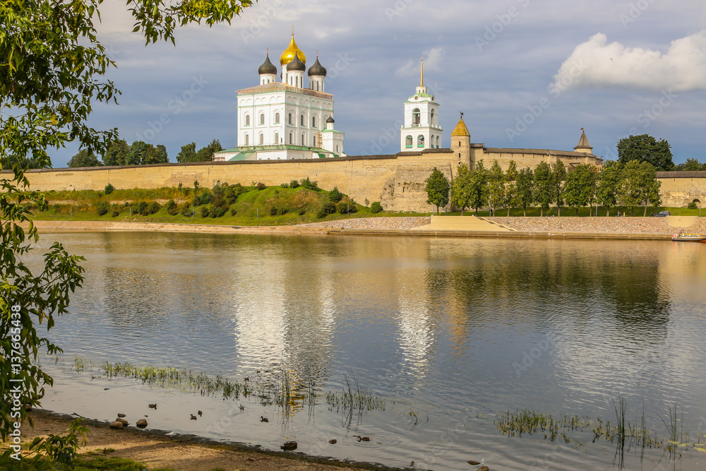 Ancient old fortress on the river bank bright clouds sky July, Russia - Pskov Kremlin wall, Trinity Cathedral, Bell Tower and Dovmontova (Smerdya) tower at the sunset. View from the Velikaya river