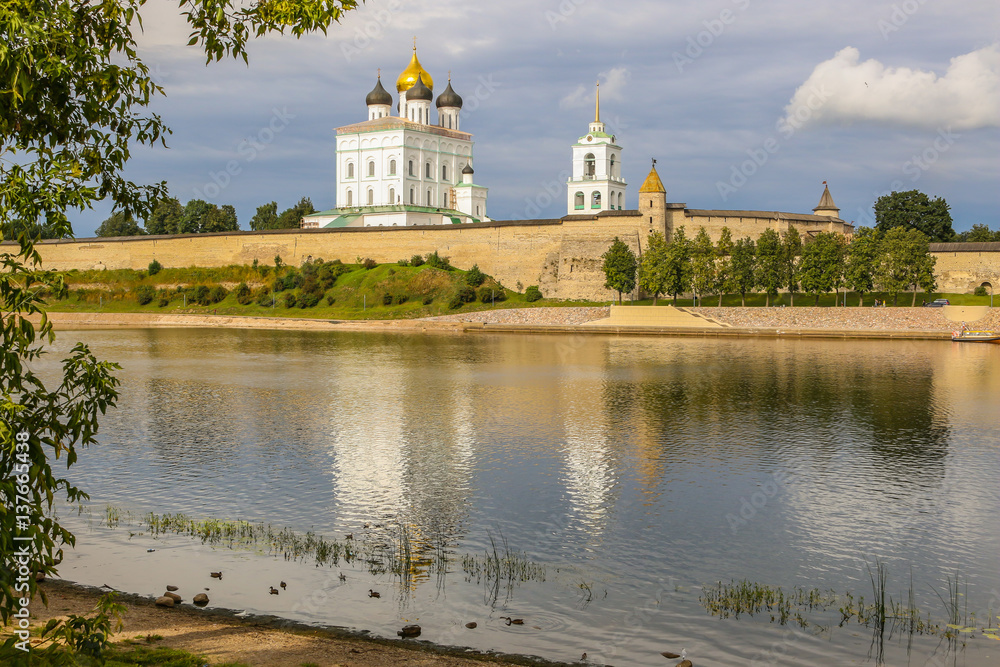Ancient old fortress on the river bank bright clouds sky July, Russia - Pskov Kremlin wall, Trinity Cathedral, Bell Tower and Dovmontova (Smerdya) tower at the sunset. View from the Velikaya river Ancient old fortress on the river bank bright clouds sky July, Russia - Pskov Kremlin wall, Trinity Cathedral, Bell Tower and Dovmontova (Smerdya) tower at the sunset. View from the Velikaya river