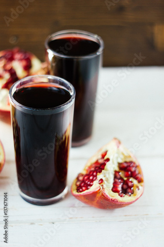 Pomegranate juice in glass surrounded by pomegranate halves.