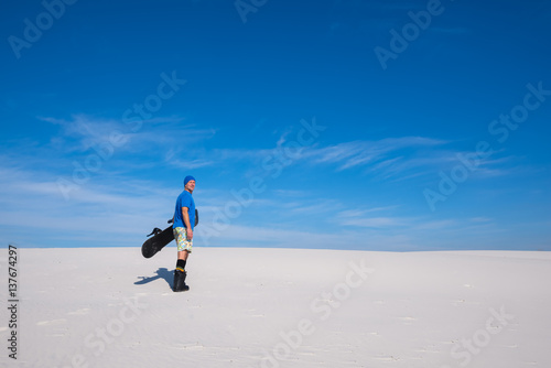 Happy man with a snowboard in hands stands in on the sand dune