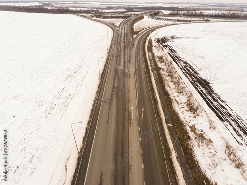 Snowy and frozen winter road with a moving car on it. Aerial view.