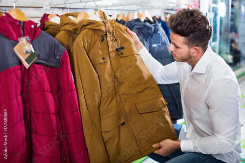 Young man choosing new coat in sports store