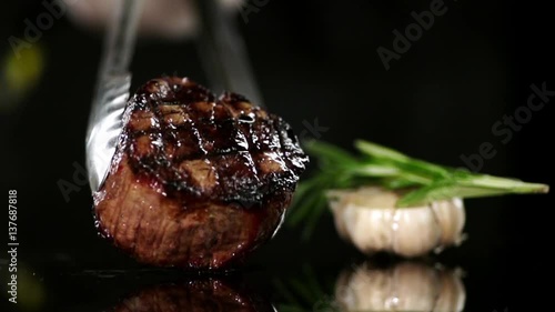 CLOSE UP FOOD: Cooking tongs put filet mignon on a black surface slow motion