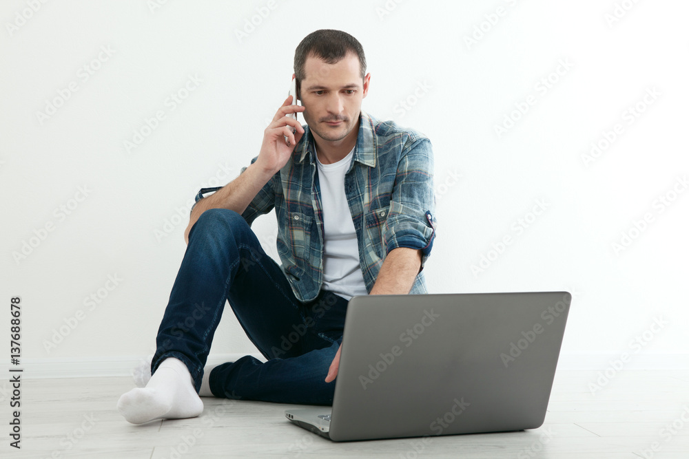 Young handsome man relaxing on floor and using laptop, smart phone at home.