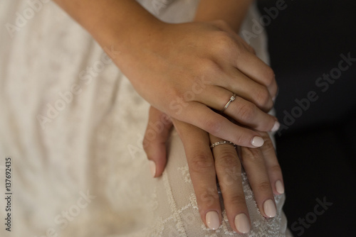 Hands of bride with rings with diamonds and beige manicure closeup on wedding dress