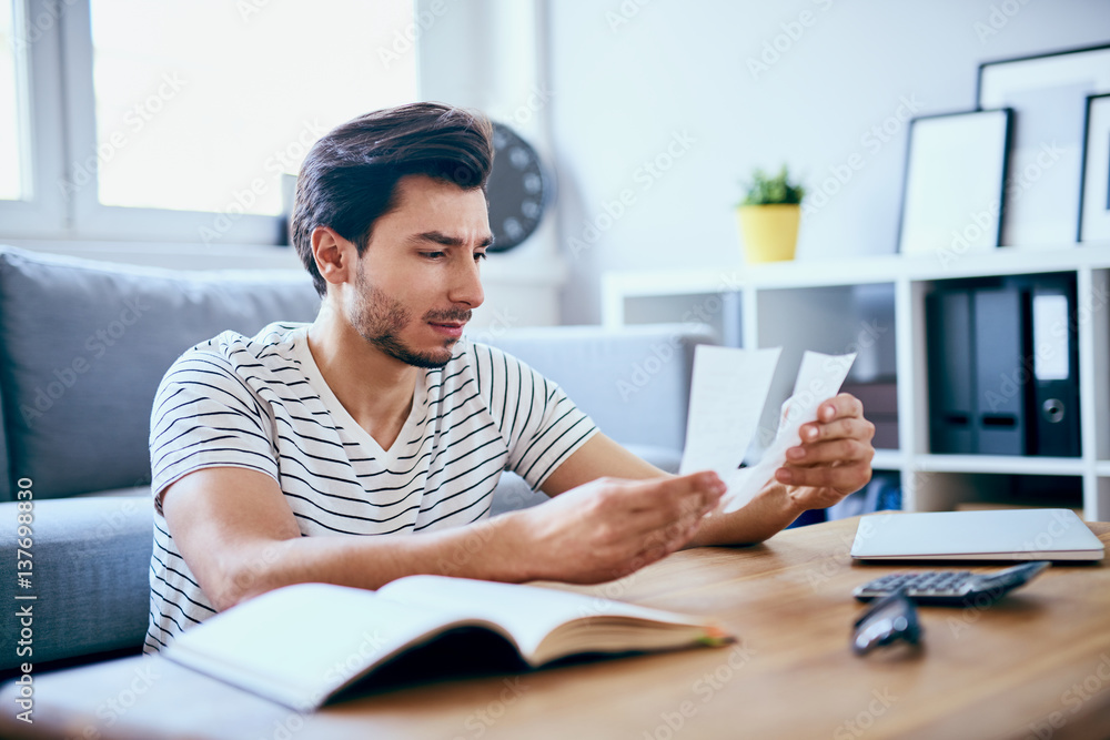 Obraz premium Unhappy man looking at bills sitting at table in living room
