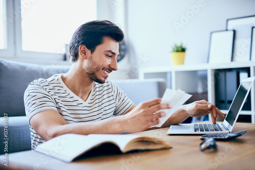 Happy man paying bills on his laptop in living room photo