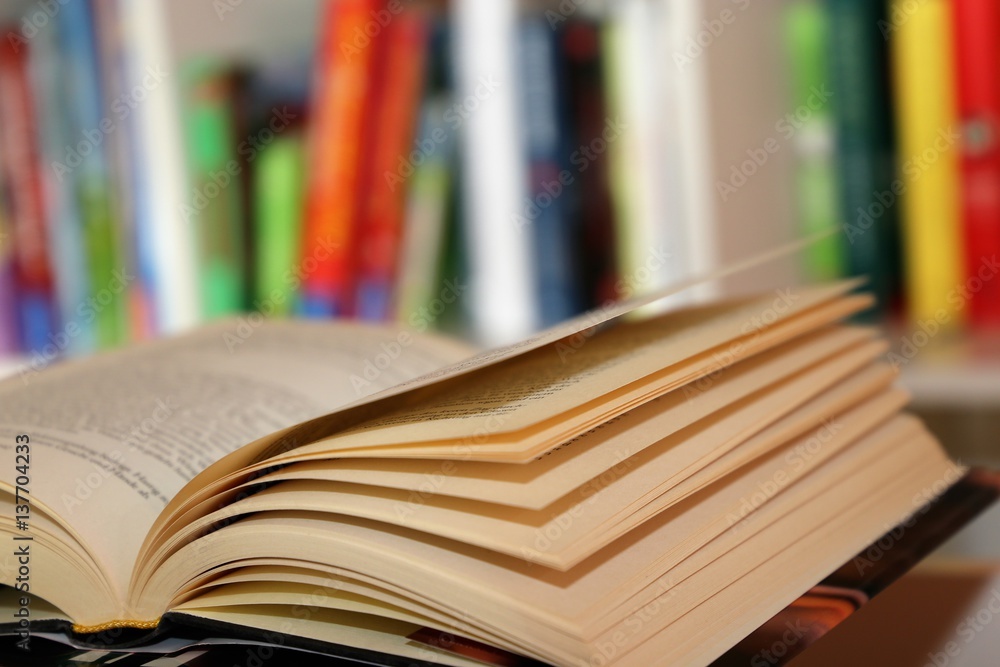 Aufgeschlagenes Buch vor einem Bücherregal Aufgeschlagenes Buch vor einem Bücherregal