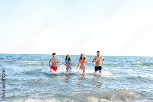 four happy friends young people man and woman having fun at ocean beach jumping together in the sea