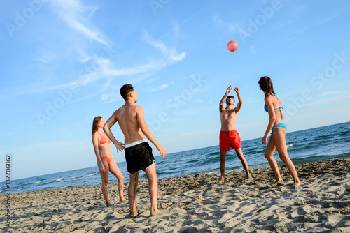 four young people man and woman playing beach volley together by the sea in sunny summer vacation day