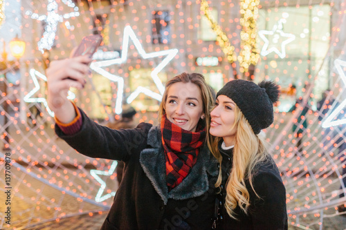 Girls walk and have a good time. They have stopped to take a selfie. Girls very beautifully look against the background of bright fires.