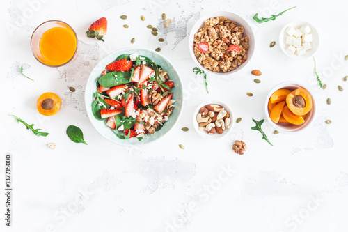 Breakfast with muesli, strawberry salad, fresh fruit, nuts on white background. Healthy food concept. Flat lay, top view