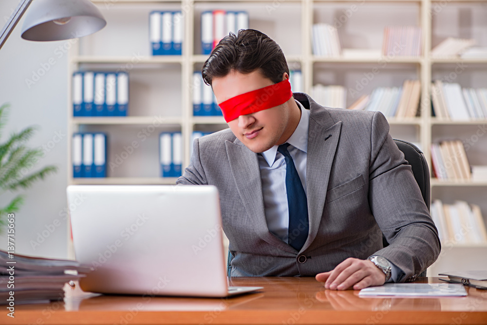 Blindfold businessman sitting at desk in office Blindfold businessman sitting at desk in office