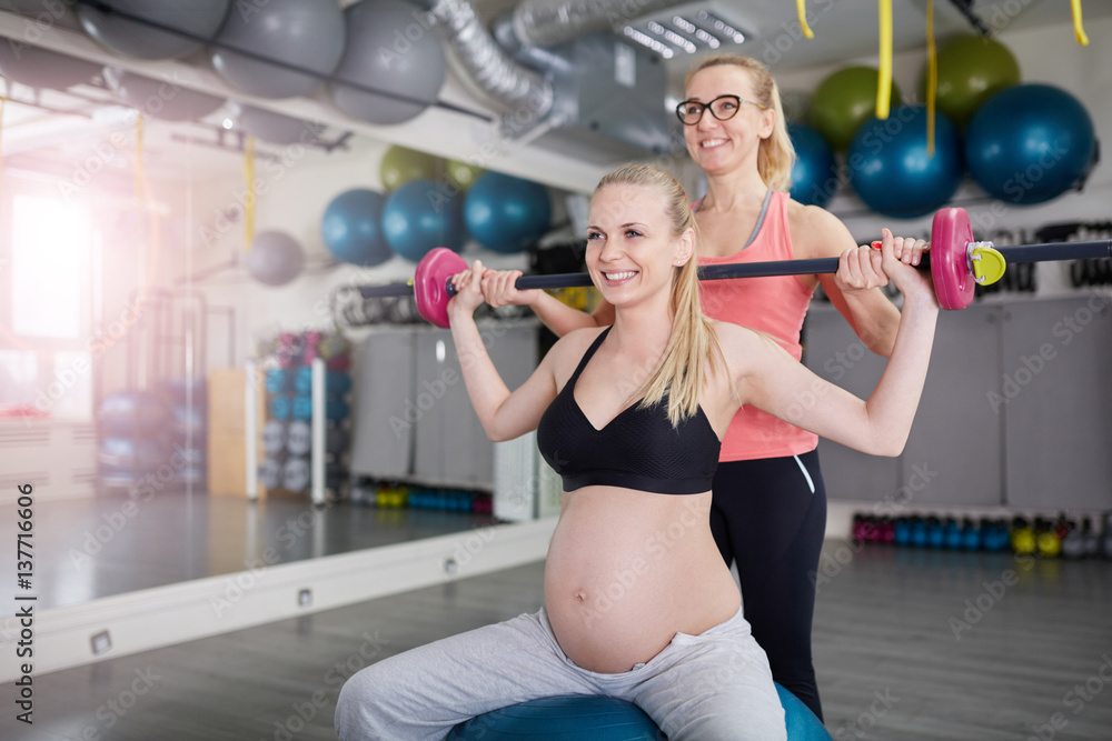 Happy pregnant woman lifting barbell with her personal coach Happy pregnant woman lifting barbell with her personal coach