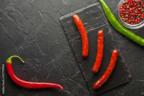 grilled sausages with chili pepper on black stone background
