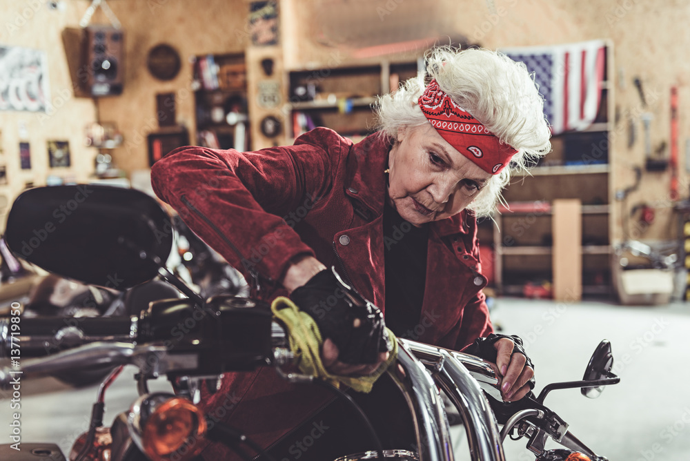 Calm female pensioner rubbing bike in garage