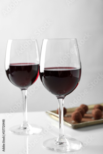 Glasses with red wine and chocolate truffles on background