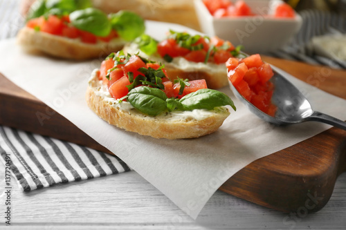 Delicious bruschetta with chopped tomatoes and basil on parchment, closeup