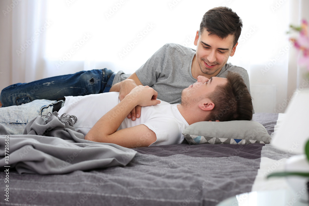 Happy gay couple lying on bed at home