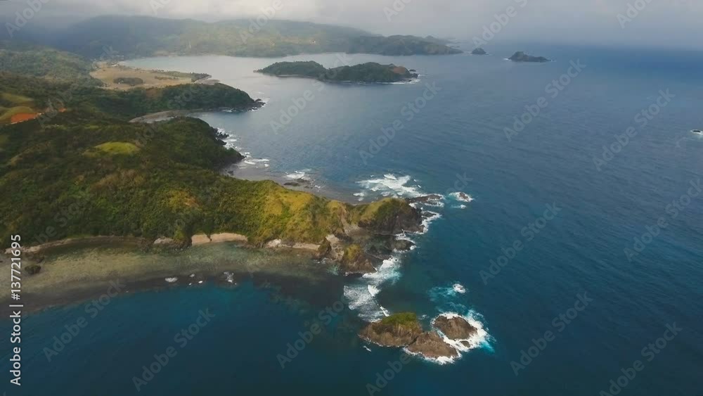 The coast of the tropical island with the mountains and the rainforest on a background of ocean with big waves.Aerial view: sea and the tropical island with rocks, beach and waves. Seascape: sky The coast of the tropical island with the mountains and the rainforest on a background of ocean with big waves.Aerial view: sea and the tropical island with rocks, beach and waves. Seascape: sky