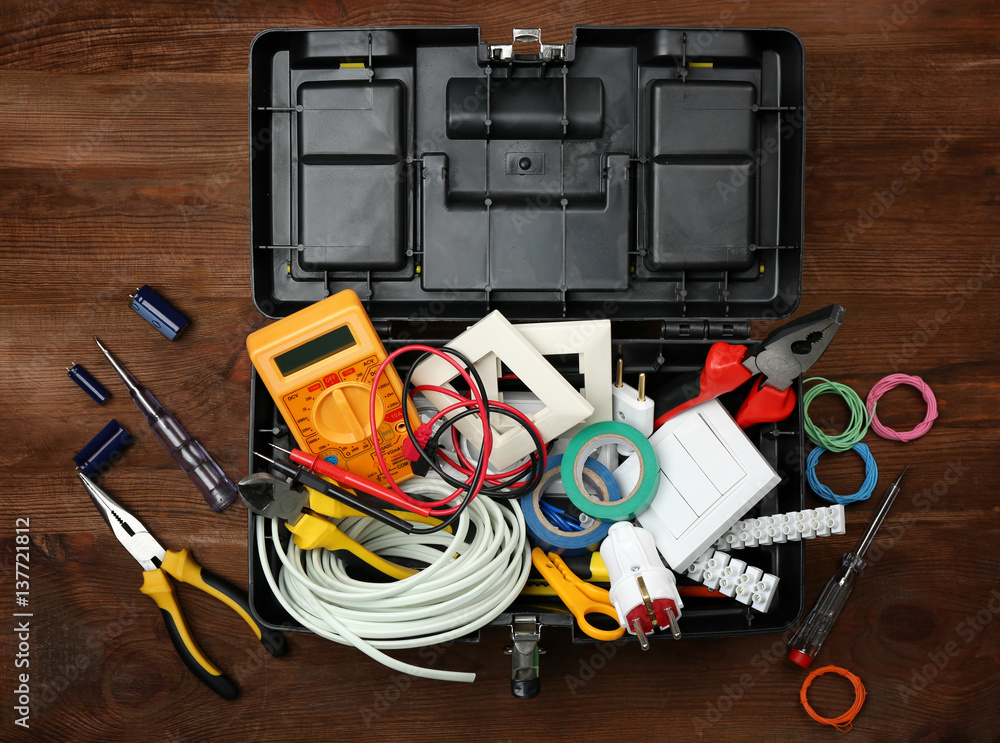 Box with electrician tools on wooden background