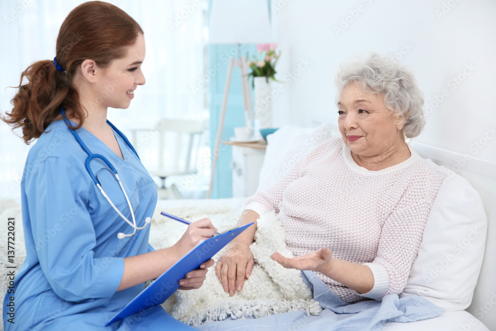 Fototapeta premium Nurse talking with elderly woman in light room