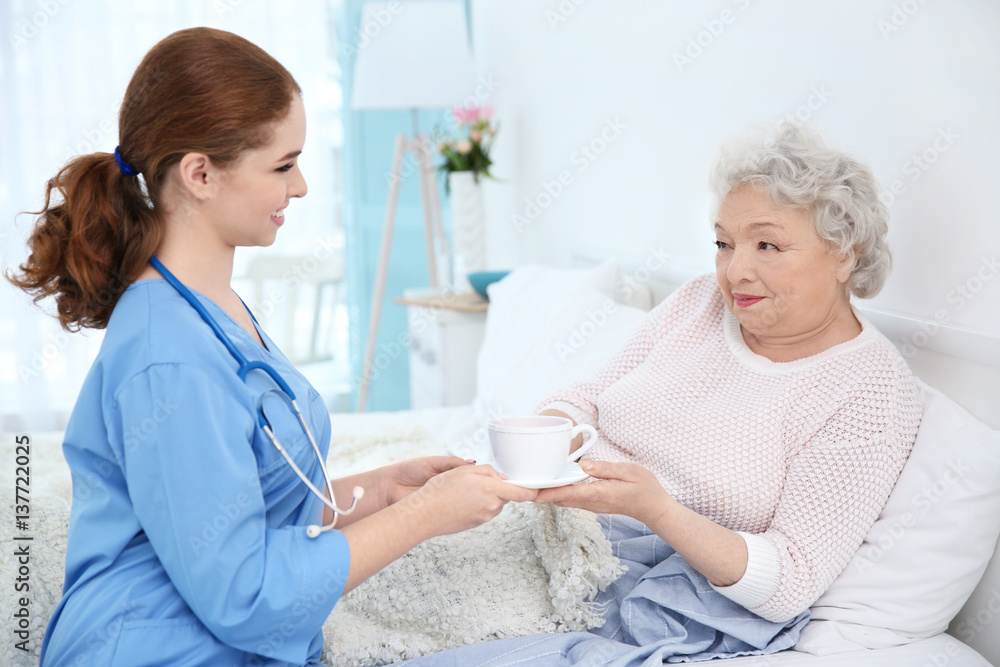 Nurse giving to elderly woman cup of tea in light room Nurse giving to elderly woman cup of tea in light room