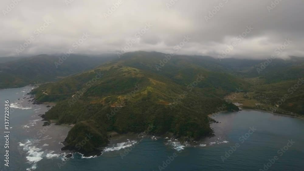 The coast of the tropical island with the mountains and the rainforest on a background of ocean with big waves.Aerial view: sea and the tropical island with rocks, beach and waves. Seascape: sky The coast of the tropical island with the mountains and the rainforest on a background of ocean with big waves.Aerial view: sea and the tropical island with rocks, beach and waves. Seascape: sky
