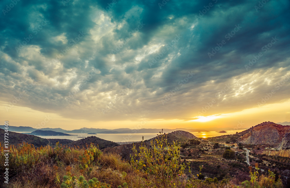 Colorful sunset view of mountains and sea and dramatic clouds on Aegina island, Greece.