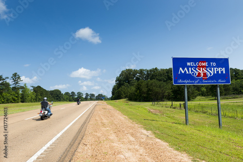 Two motorcycles passing by the Mississippi State welcome sign along the US Highway 61 in the USA; Concept for travel in America and Road Trip in America