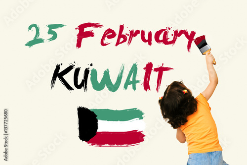 Cute little girl writing KUWAIT National Day25 February with Kuwait Flag using painting brush on wall background photo