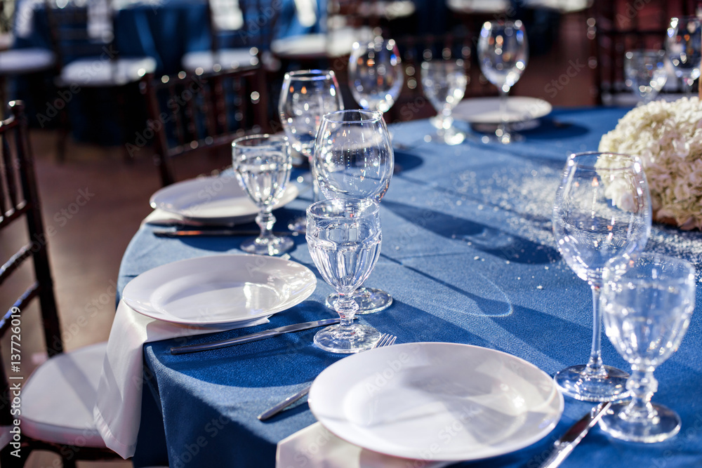 Wedding. Banquet. The chairs and round table for guests, served with cutlery and crockery and covered with a blue tablecloth.