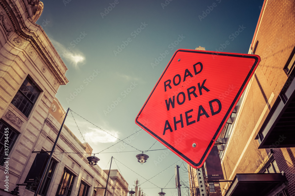 Obraz premium Road Work Ahead Orange Street Sign In City
