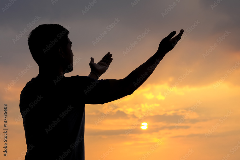 silhouette of a man with hand up on sunset background, The concept the blessings from heaven