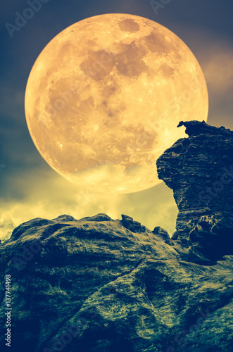 Boulder against sky with clouds and beautiful super moon at night. Outdoors. Sepia tone.