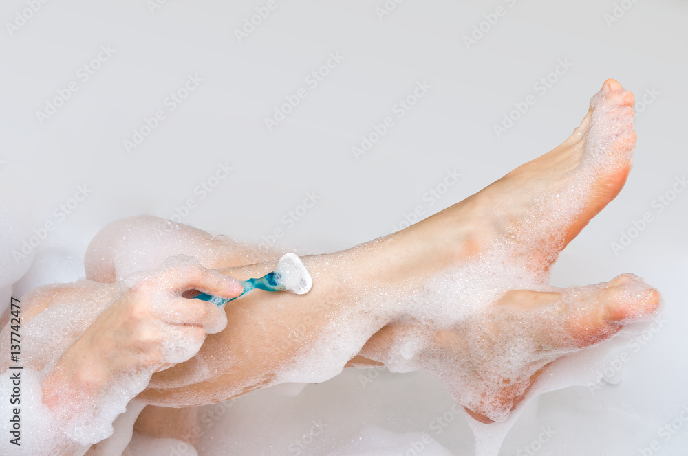 Fototapeta premium Woman shaving legs with razor in bathroom