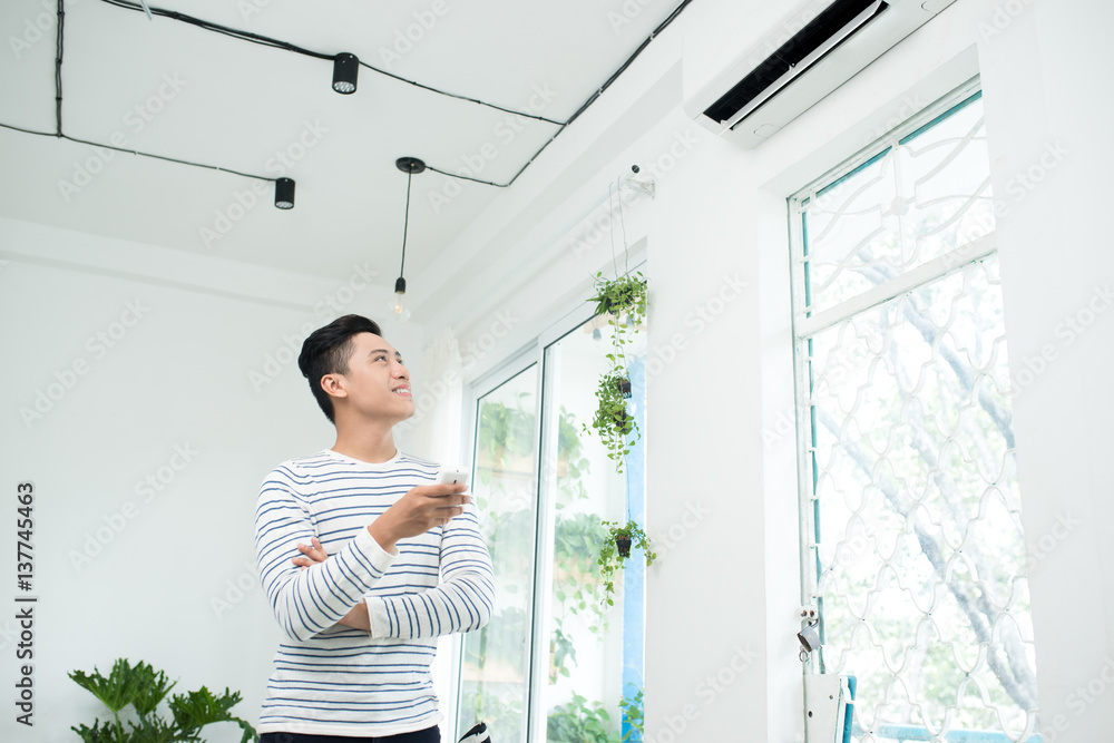 Asian man is turning air condition by remote control and smiling Asian man is turning air condition by remote control and smiling