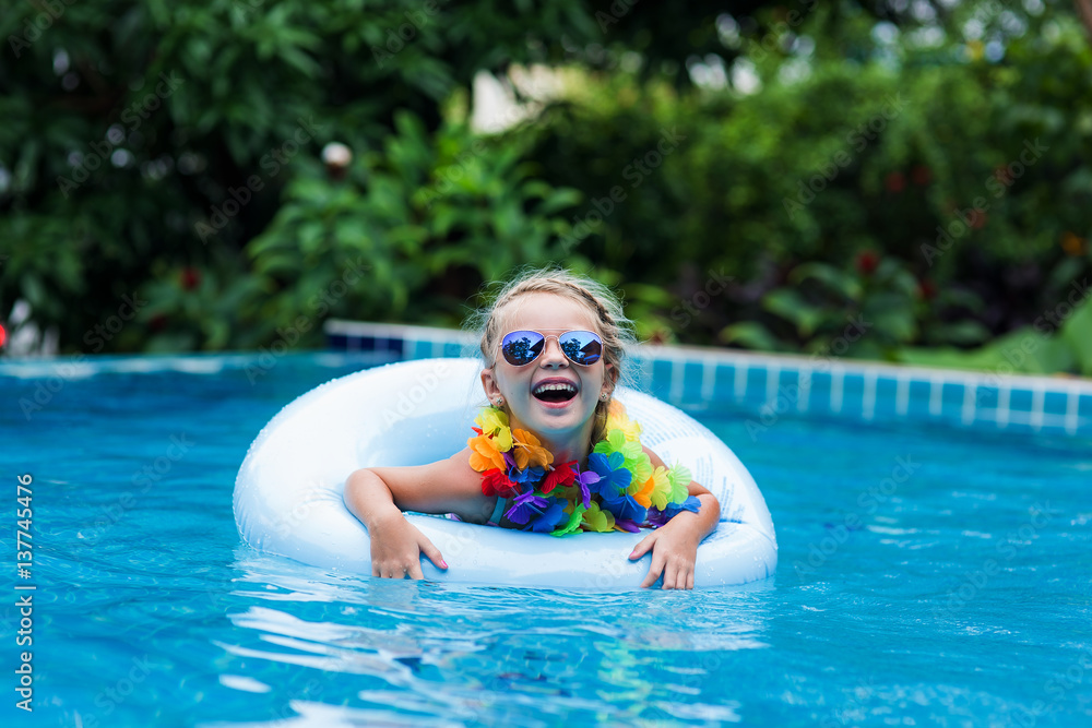 little girl in sunglasses floating on the circle in the pool at a resort in the tropics