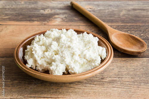 Cottage cheese in the dish on the wooden table in the kitchen. Healthy eating and lifestyle.