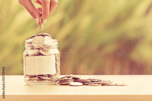 Fényképezés Hand putting Coins in glass jar with blank label for giving and donation concept