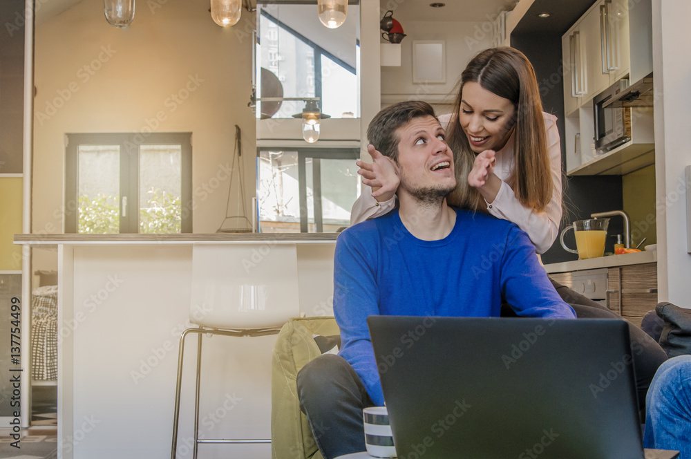 Happy couple doing business together working at small office at home, Portrait of a cheerful woman hugging man from behind Happy couple doing business together working at small office at home, Portrait of a cheerful woman hugging man from behind