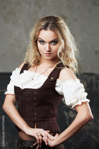 Portrait of a beautiful steampunk woman in a pant suit with vest, over grunge background.