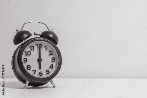 Closeup alarm clock for decorate in 6 o'clock on white wood desk and cream wallpaper textured background in black and white tone with copy space