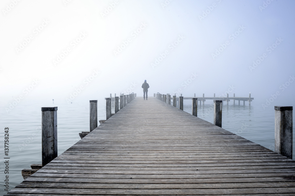 Mann auf Holzsteg im Nebel am Wasser