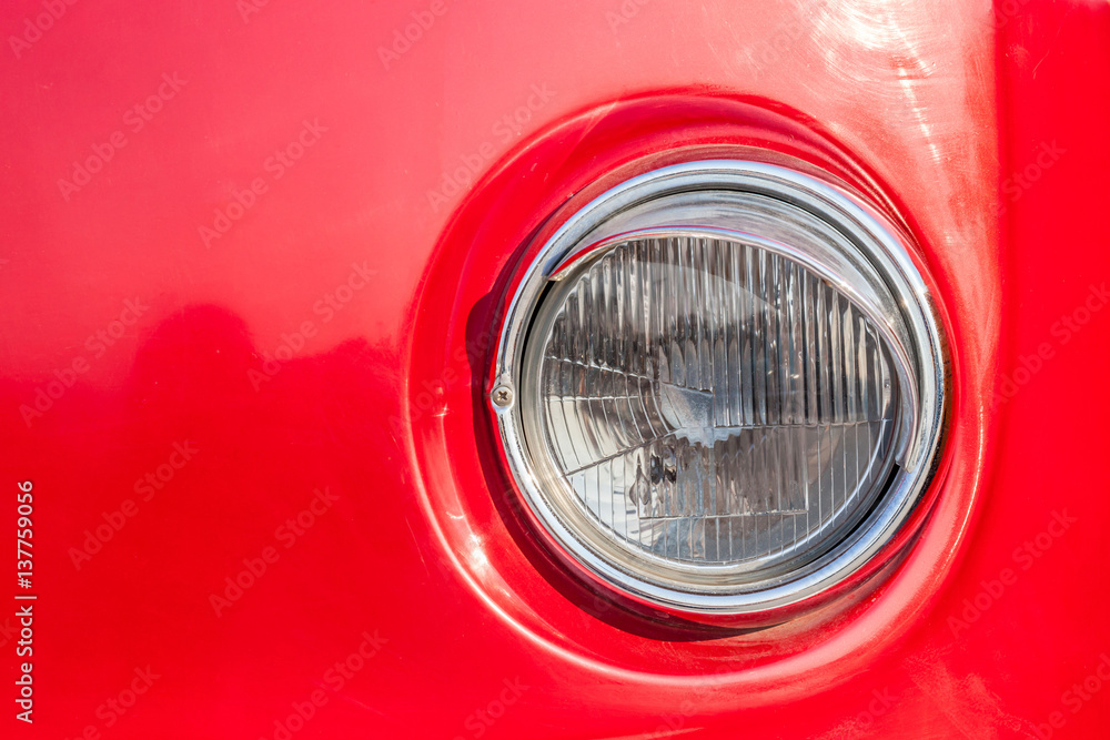 Close-up round headlight of shiny red vintage retro car.