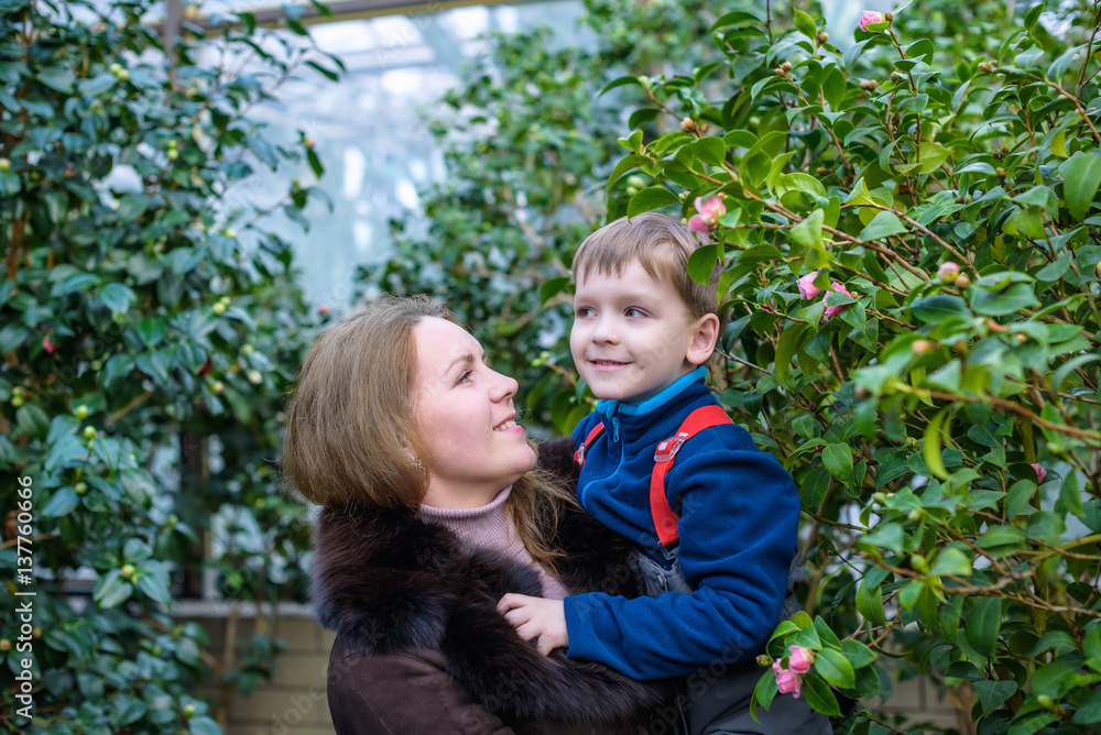 Beautiful woman holding her little adorable kid boy in the blooming park on a sunny spring day. Happy mother with her son enjoying azalea trees flowers. Mum and child outdoors